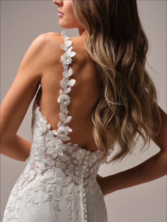 Back view of the Isoline wedding dress highlighting the illusion bodice, open back with floral lace detailing, delicate lace straps, and covered button closure.