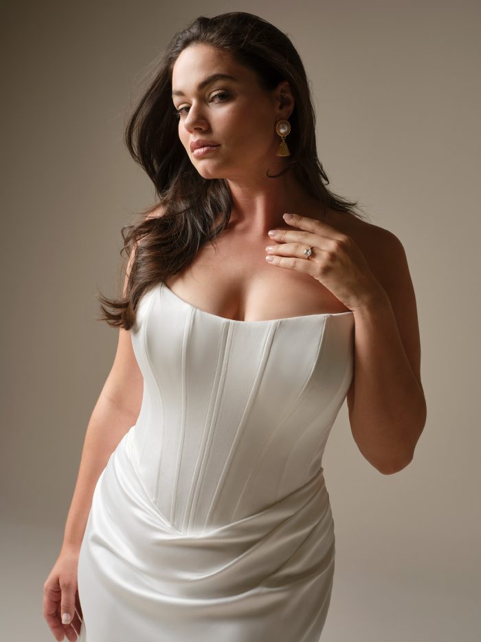 Close-up of Sinclaire by Maggie Sottero — plus-size strapless satin wedding gown featuring structured corset seams, gentle ruching at the hips, and romantic sweetheart neckline.