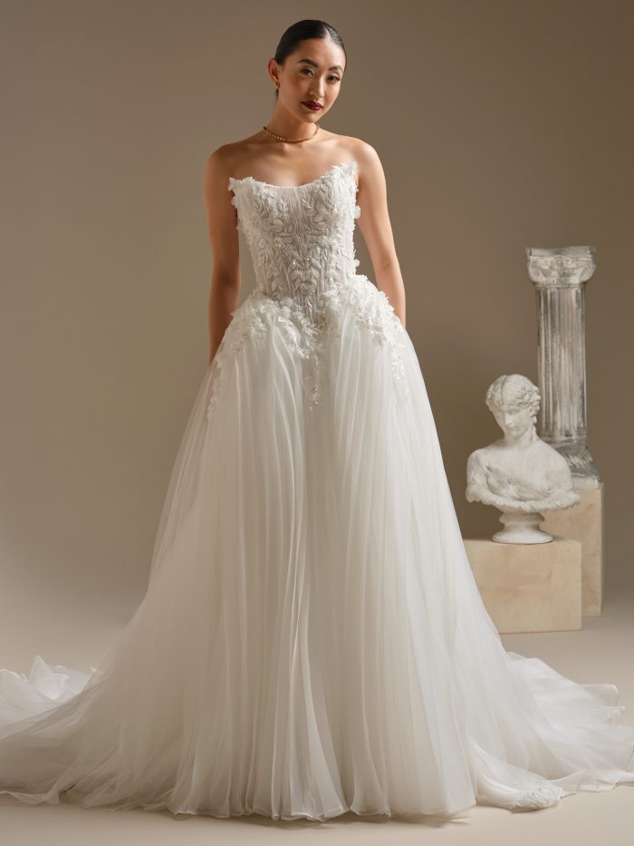 Bride wearing the Jayna ballgown wedding dress featuring a cat-eye strapless neckline, dimensional 3D floral lace bodice, and a pleated glitter tulle skirt with full princess volume, photographed in a studio setting.