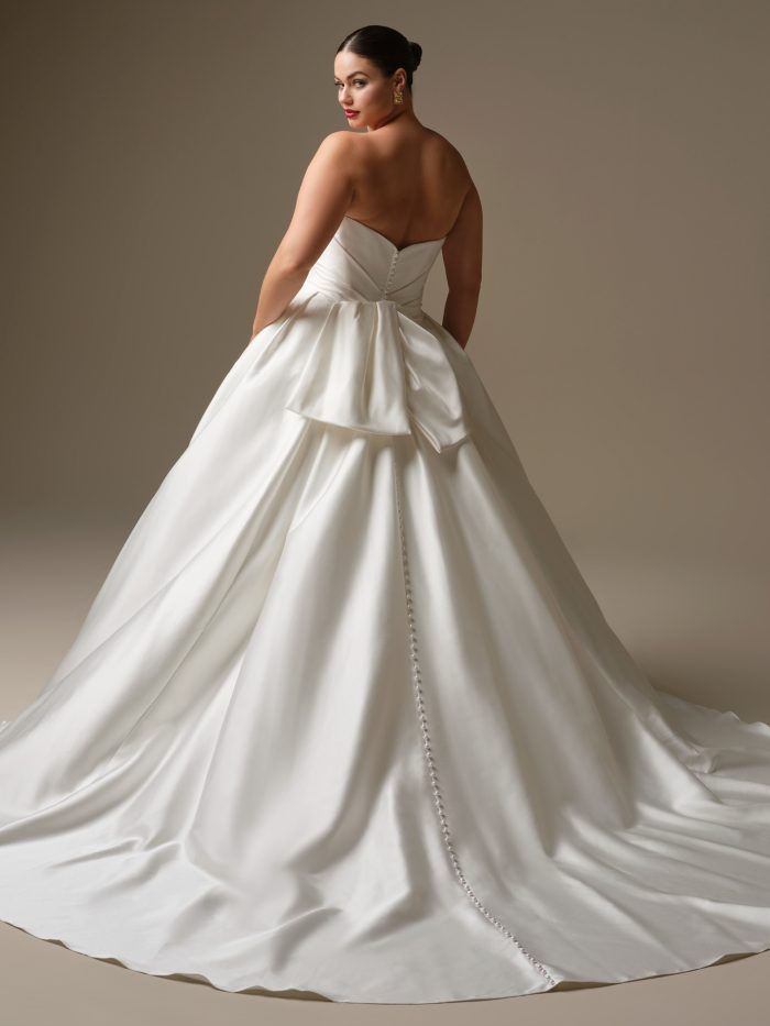 Back view of Kincaid by Sottero and Midgley — plus-size satin ballgown wedding gown featuring dramatic bow detail, full pleated train, and line of satin buttons down the back.