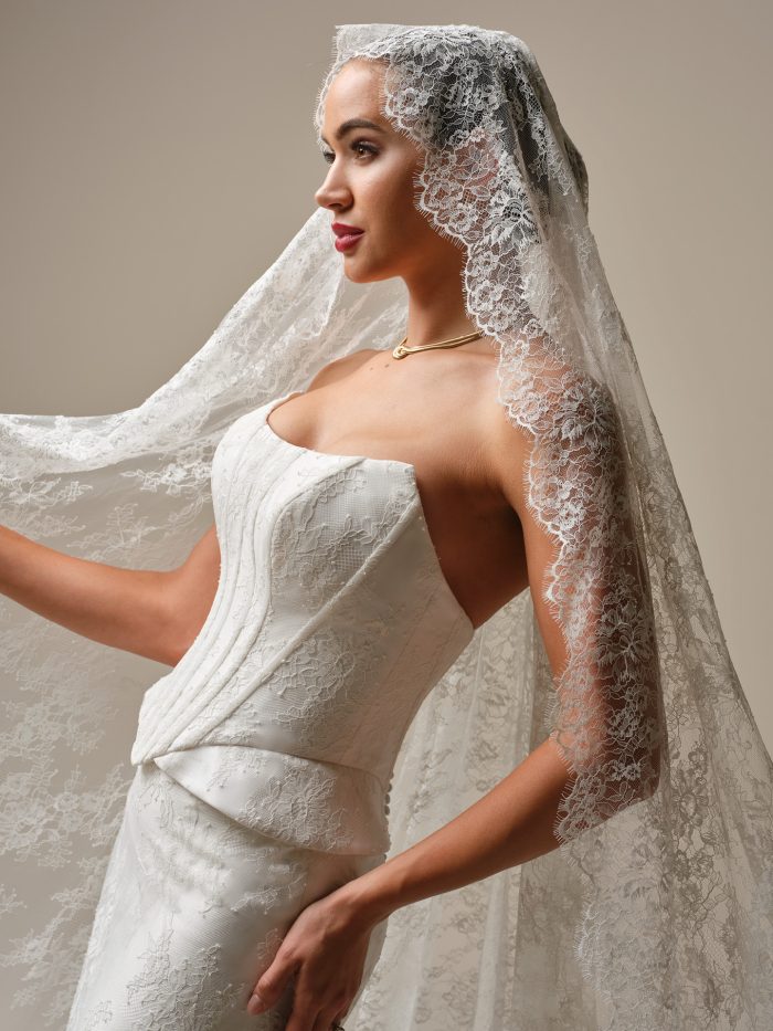Side view of the Lassen wedding dress highlighting the strapless cat-eye neckline, structured corset bodice, peplum waist detail, and matching Chantilly lace veil for a vintage-inspired look.