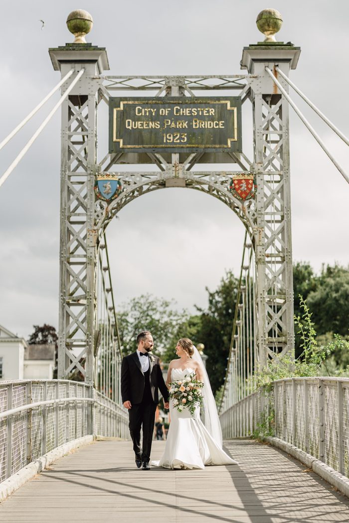 Bride walking across a bridge with her husband wearing a vintage wedding dress with a cathedral veil