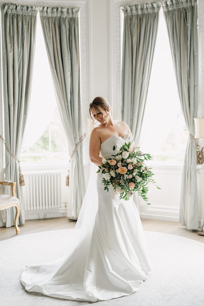 Bride holding a flower bouquet in a bridal suite wearing a modern and simple mermaid wedding dress