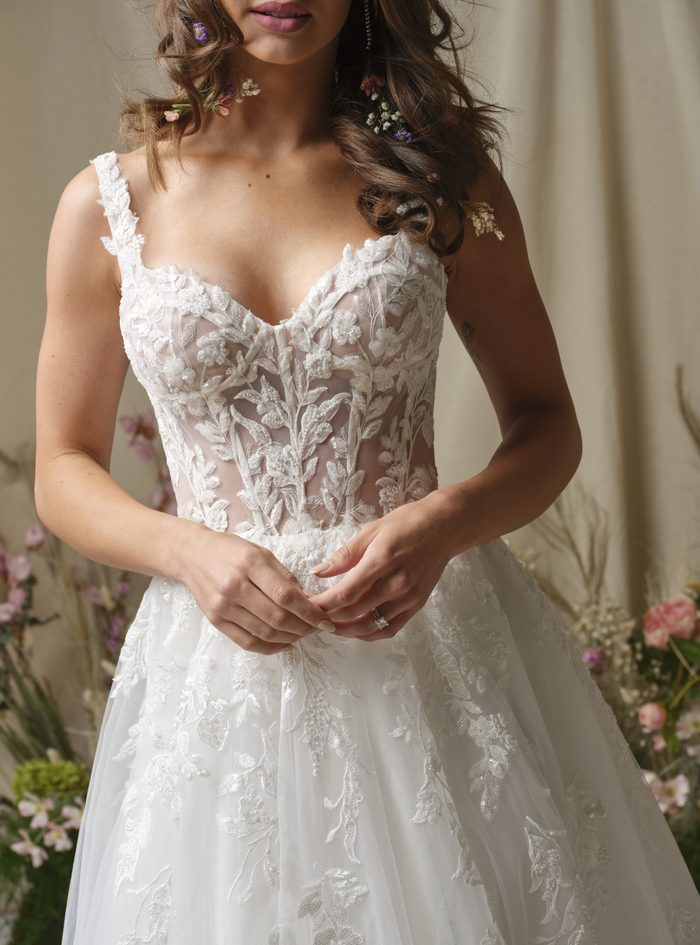 Close-up detail of the Susan ball gown wedding dress by Rebecca Ingram, showing a sheer illusion bodice with floral lace appliqué and beaded straps over a sweetheart neckline, with a lace and tulle ball gown skirt.