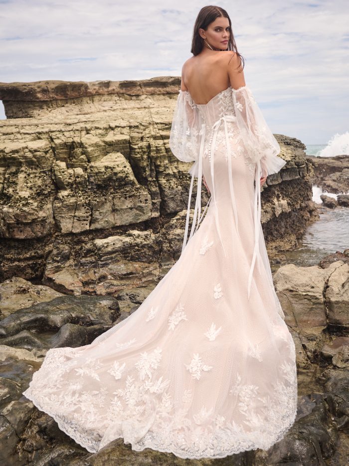 Back view of the Connor wedding dress by Sottero and Midgley showing an open back with lace-up corset detail, organza ties with pearl-accented ends, and a fitted lace skirt with train