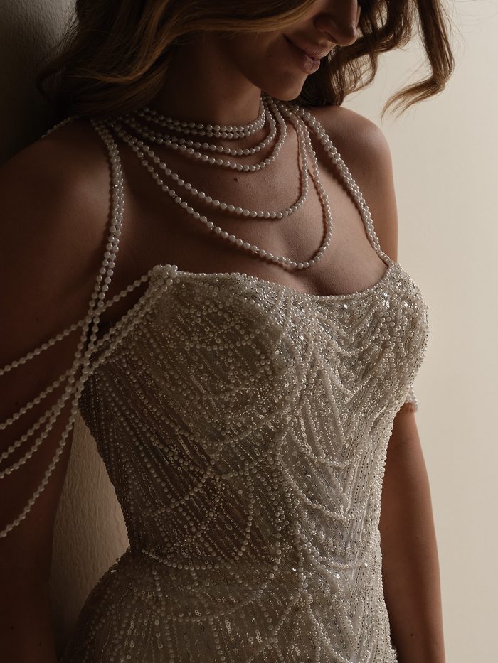 "Close-up detail of the Constance sheath wedding dress bodice by Sottero and Midgley, showing dense sequin and pearl beading in a chevron pattern with layered draped pearl necklace straps.