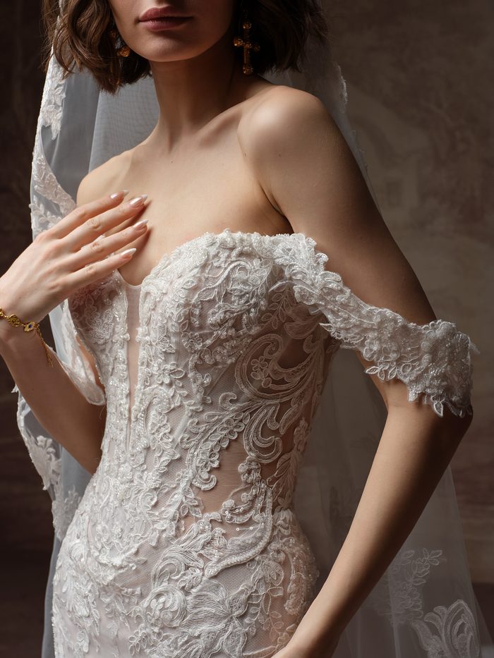 Close-up detail of the Julianna wedding dress and cap sleeves by Sottero and Midgley, showing intricate paisley lace appliqué over an illusion bodice with scalloped off-the-shoulder sleeves.