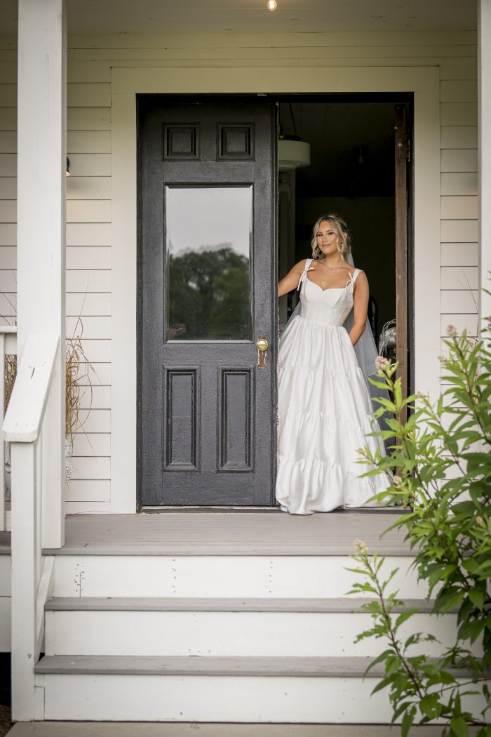 Bride walking out the front door wearing her simple tiered wedding dress with bow ties