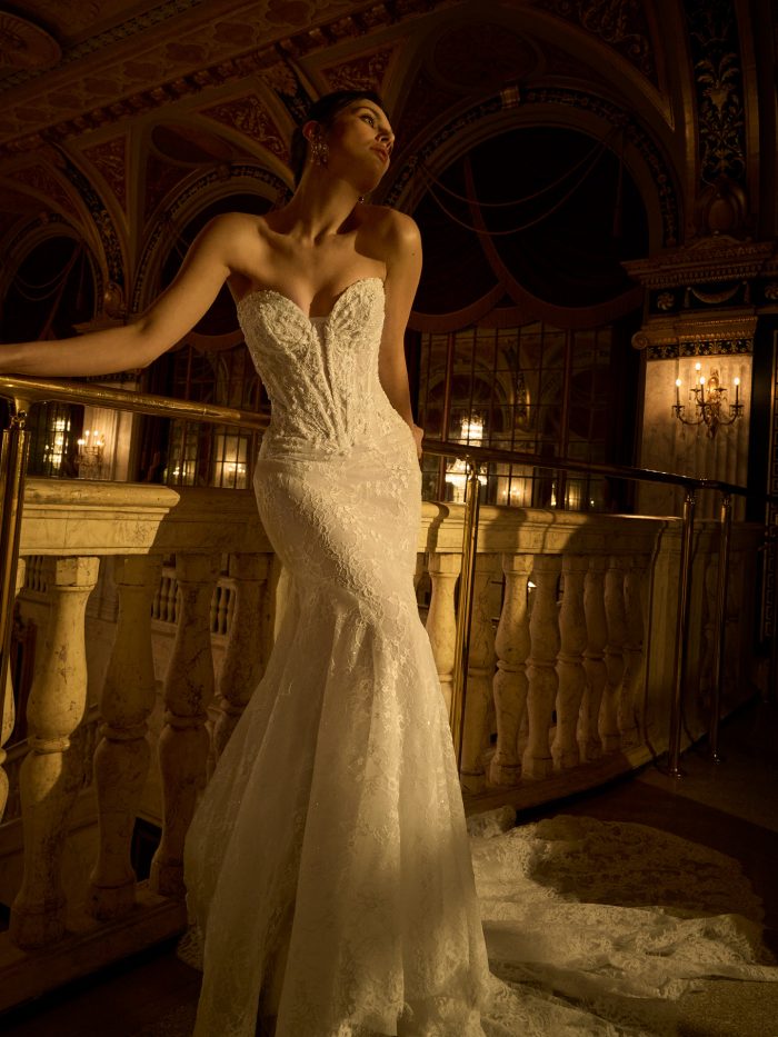 Maggie Sottero Bellevue Royale fit-and-flare wedding dress with a sweetheart neckline and structured lace bodice, flowing into a fitted silhouette and lace train, photographed in a grand, softly lit interior.