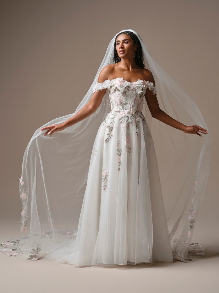 Bride wearing the Blossom veil by Rebecca Ingram, a cathedral-length veil with soft tulle and delicate pink and green floral embroidery along the edges.