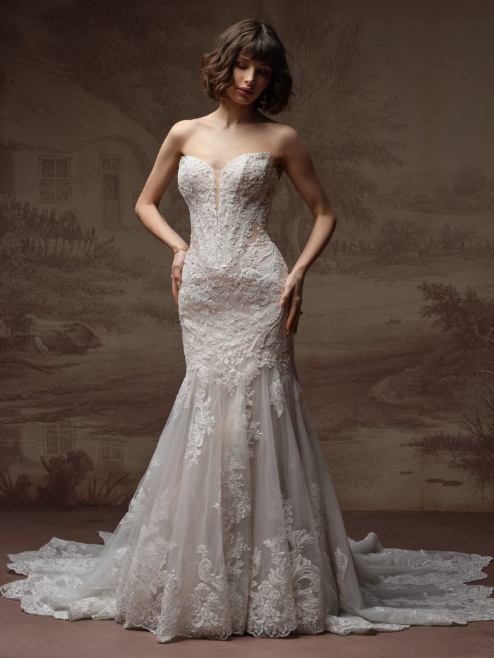 Sottero and Midgley Julianna fit-and-flare wedding dress with a plunging illusion neckline, ornate lace detailing, and a flared tulle skirt with lace train, photographed against a painterly backdrop.