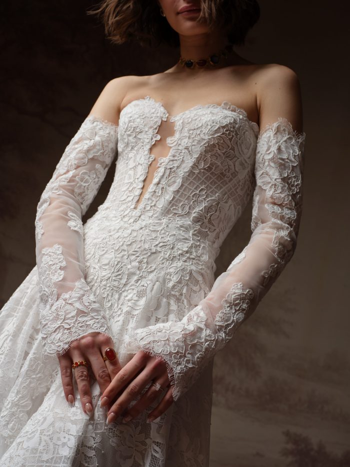 Close-up of the Sottero and Midgley Keeva's detachable sheer lace sleeves, featuring floral appliqué throughout, a scalloped raw-edge cuff, and lace-trimmed off-the-shoulder straps framing an illusion plunge bodice.