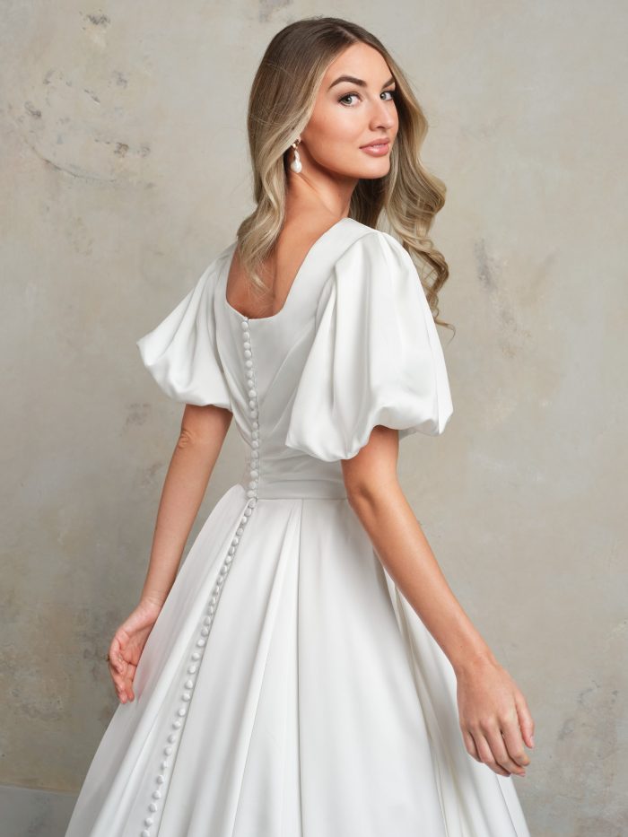 Back view of a classic satin ballgown wedding dress featuring puff sleeves, a square back neckline, and a row of covered buttons trailing to the hem.