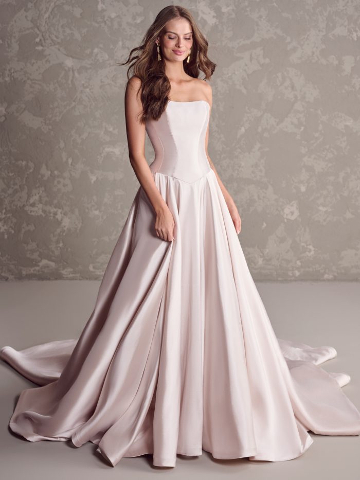 Bride wearing Maggie Sottero Emmanuelle ballgown wedding dress featuring a strapless scoop neckline, structured satin bodice, and full flowing skirt in a soft blush hue.