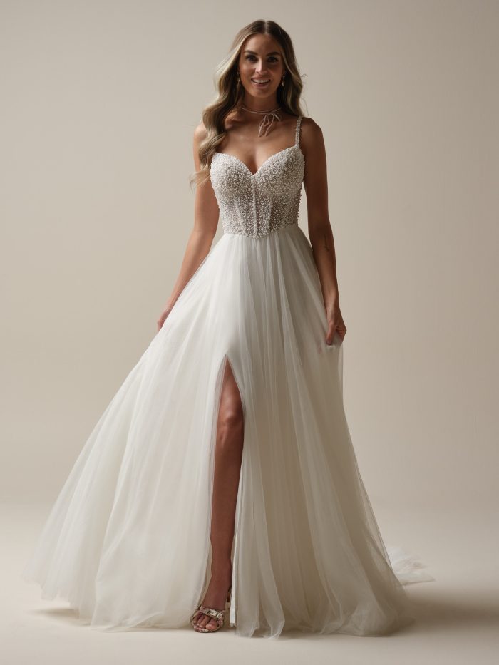 Bride wearing a romantic A-line wedding dress with a pearl-embellished bodice, spaghetti straps, and a flowing tulle skirt with a thigh-high slit.