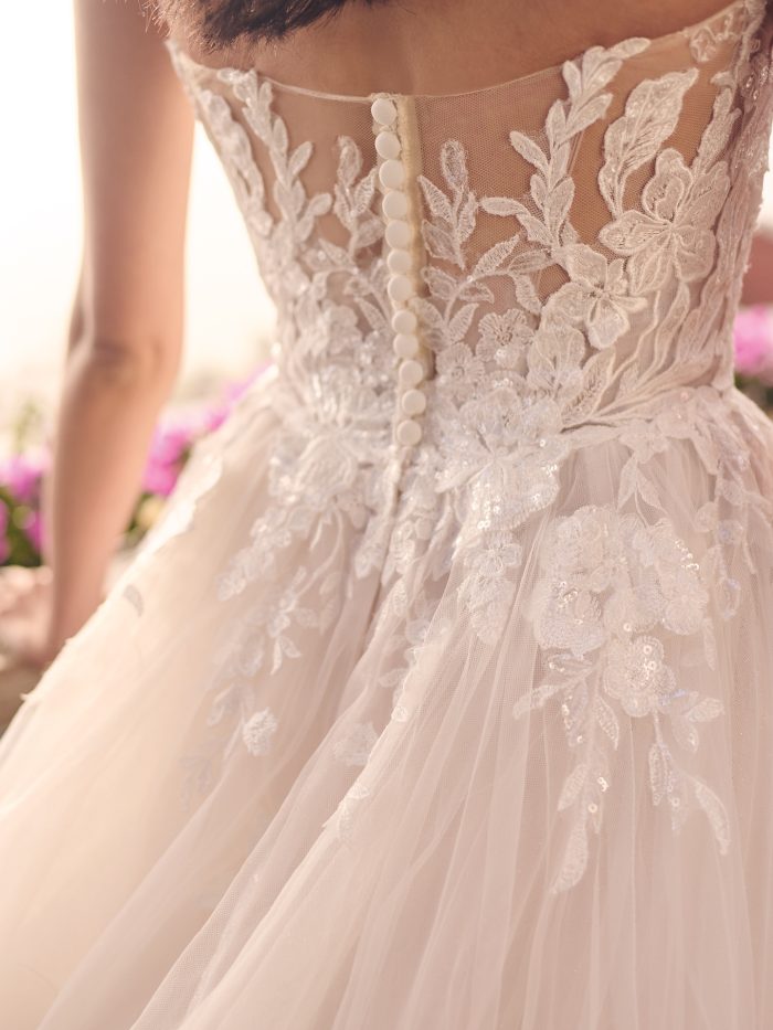 Close-up of Indiana ballgown featuring illusion lace back with button detailing, sequin floral appliqués, and soft tulle layers cascading from the waist.