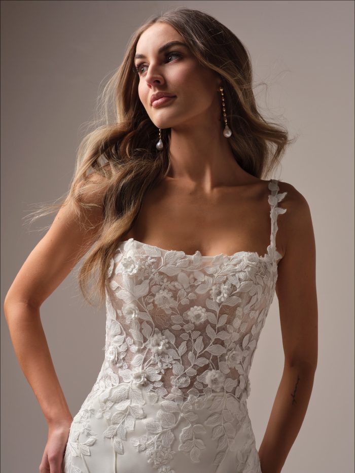 Close-up of a fit-and-flare wedding dress bodice with sheer lace overlay, floral embroidery, and 3-D appliqués along the neckline and straps for a romantic garden-inspired look.