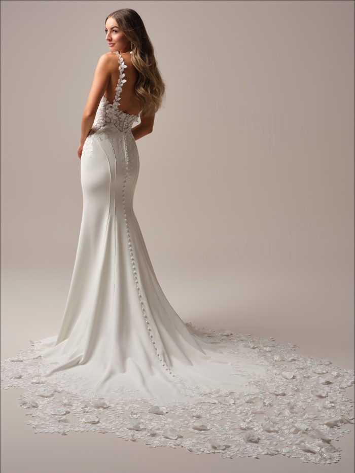 Back view of a fit-and-flare wedding dress featuring a sheer lace bodice, illusion straps with floral appliqués, and a dramatic scalloped lace train embellished with 3-D florals.