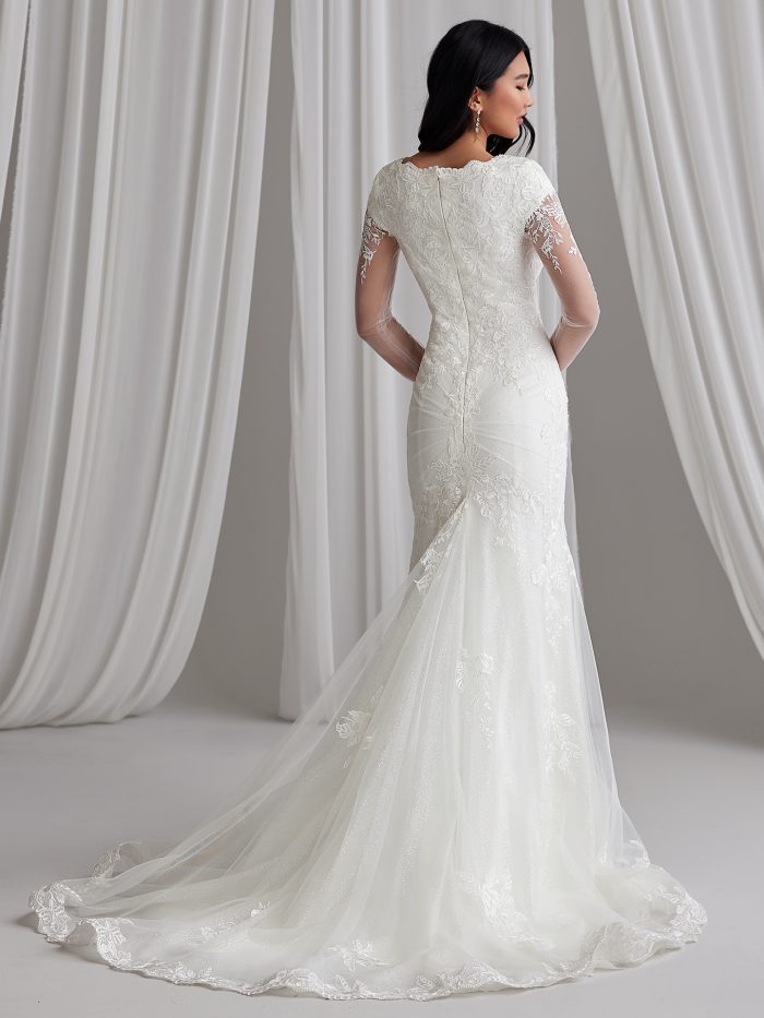 Back view of a fit-and-flare wedding dress with lace embroidery, sheer long sleeves, and a dramatic chapel train featuring a scalloped hemline.