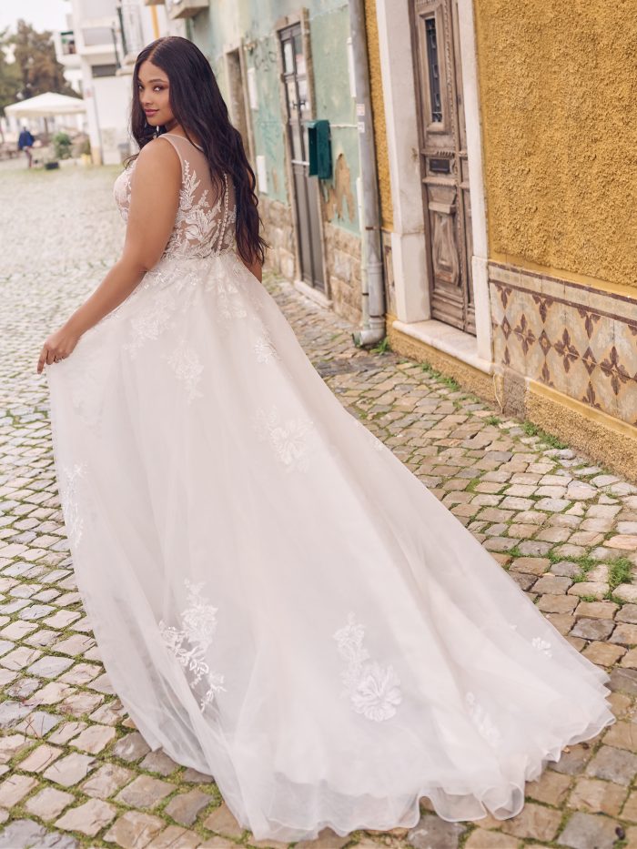 Back view of the Lindsey ball gown wedding dress, highlighting the illusion lace back, covered buttons, and flowing embroidered tulle train as the bride looks over her shoulder.