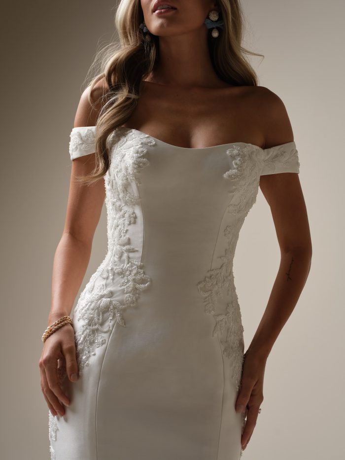 Close-up of a bride in an off-the-shoulder fit-and-flare wedding dress featuring floral lace appliqués and a softly scooped neckline.