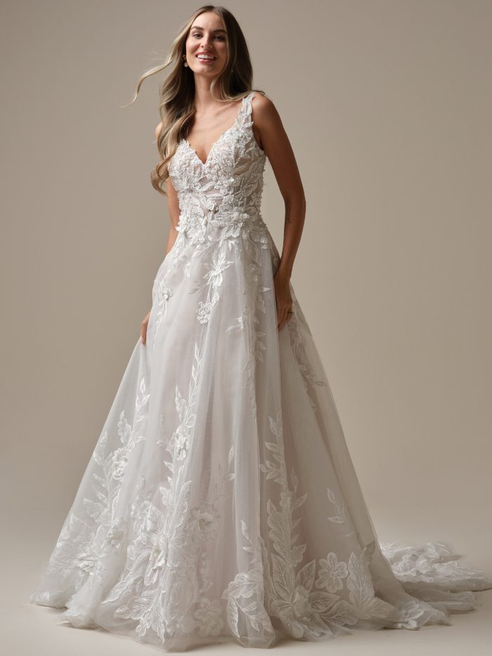 Maggie Sottero Magnolia A-line wedding dress with a plunging V-neckline, sheer bodice, and bold floral lace motifs. This romantic bridal gown features textured embroidery and a flowing tulle skirt, perfect for an ethereal wedding day look.