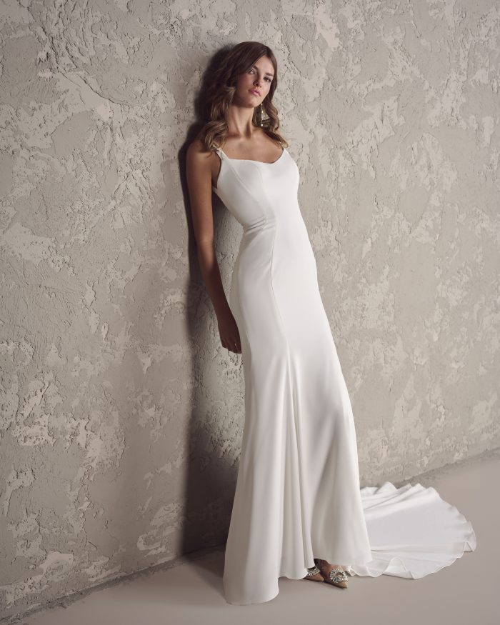 Front view of a minimalist ivory sheath wedding dress with delicate straps, soft scoop neckline, and gentle flare at the hem, styled with sparkly pointed-toe heels.
