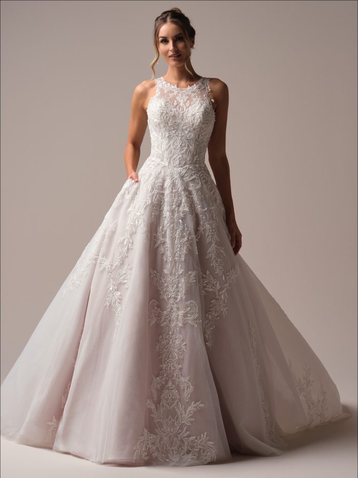 Front view of the Nina A-line gown, showcasing the illusion bateau neckline, beaded lace bodice, and full tulle skirt with ornate embroidery, worn by a smiling bride in a studio setting.