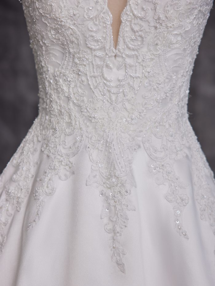 Close-up of a ballgown wedding dress bodice featuring intricate beadwork, embroidery, and a plunging illusion neckline with swirling lace appliqués over satin.