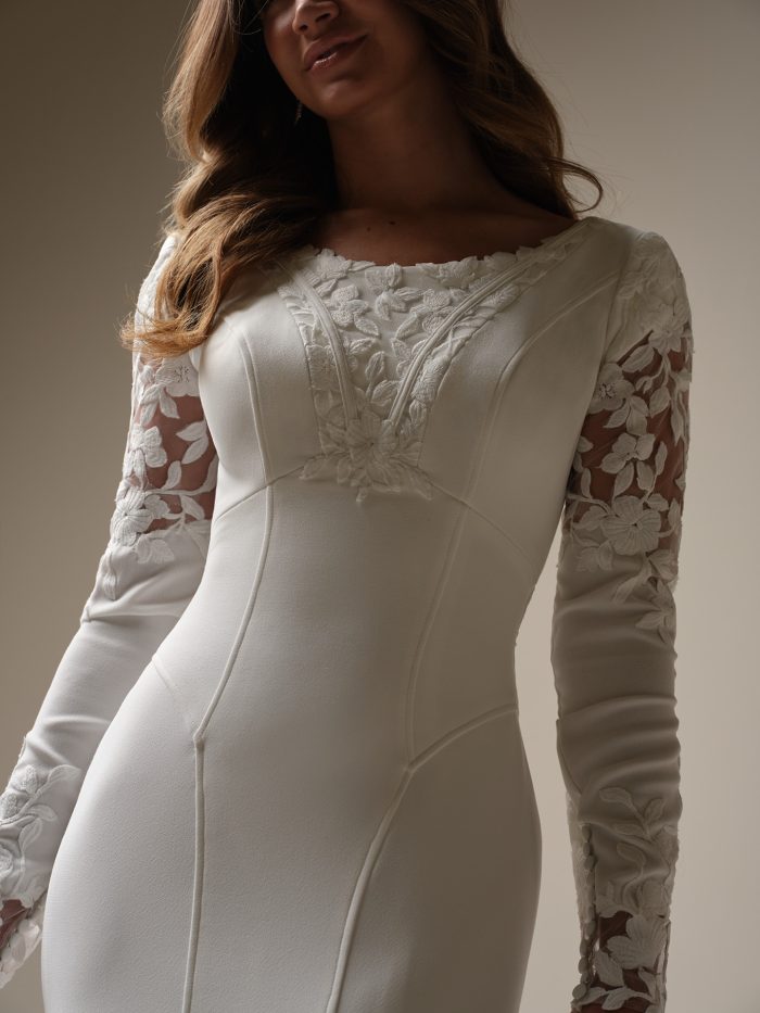 Close-up of a long sleeve wedding dress featuring a scoop neckline, floral lace appliqués on illusion sleeves, and textured embroidery on the bodice.