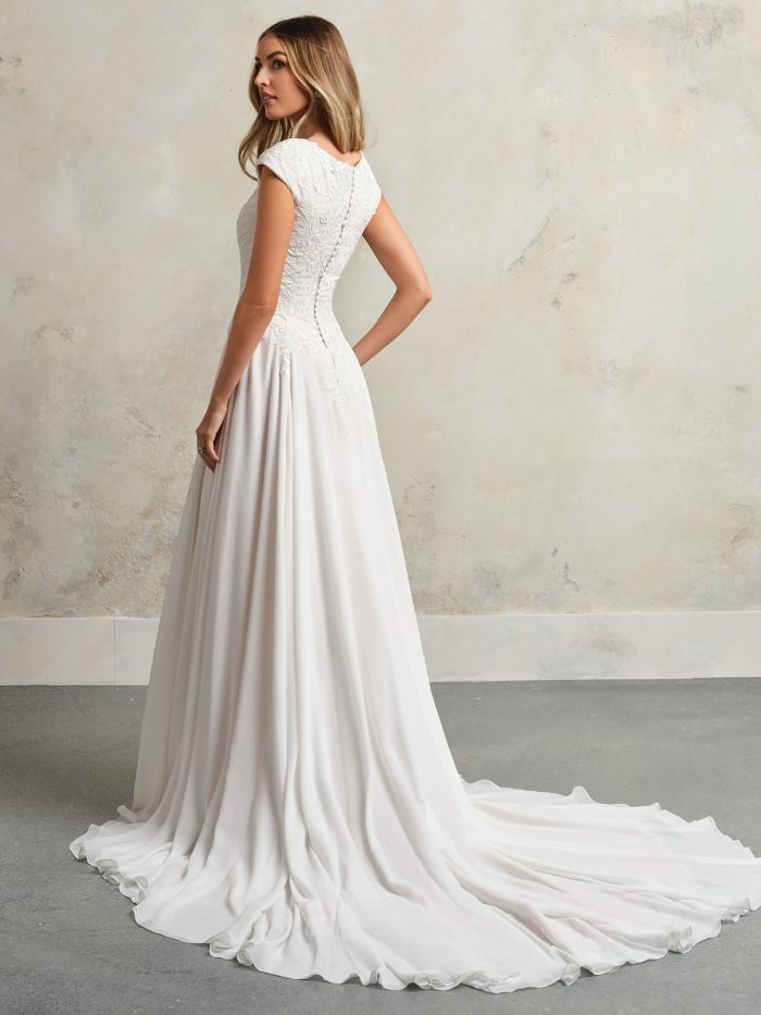 Back view of a modest sheath wedding dress with cap sleeves, lace bodice, and a flowing chiffon skirt with a soft sweep train and subtle lace detailing.