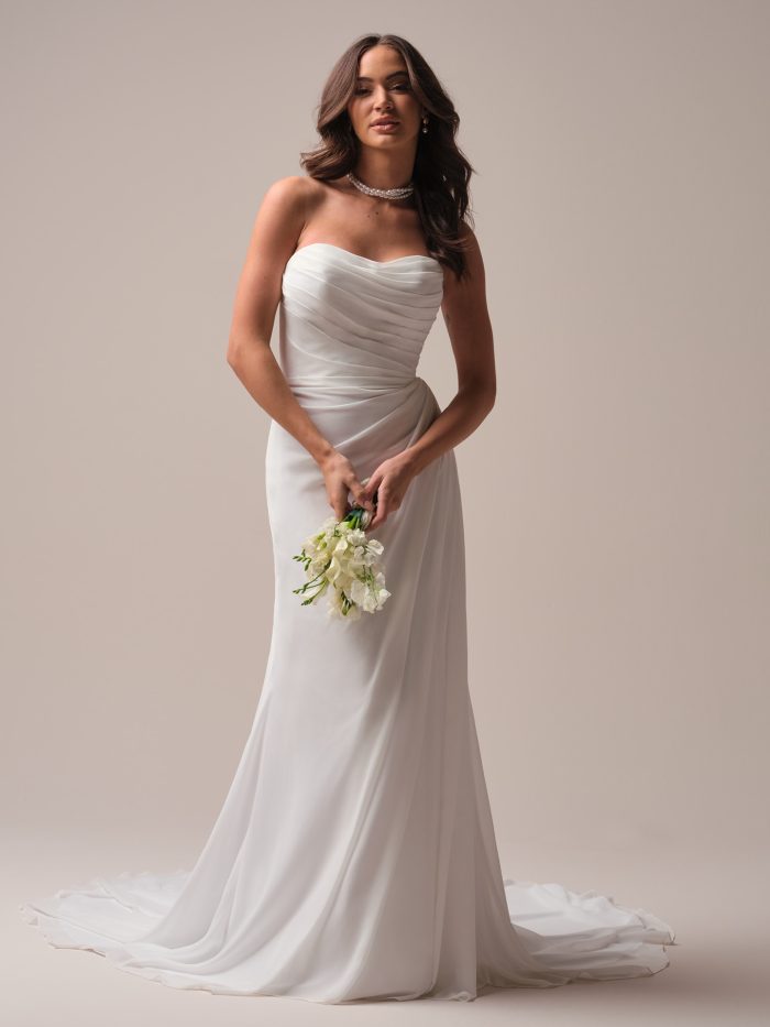 Front view of a strapless A-line wedding dress featuring a ruched sweetheart neckline and soft draped chiffon skirt, styled with a pearl choker and holding a white floral bouquet.
