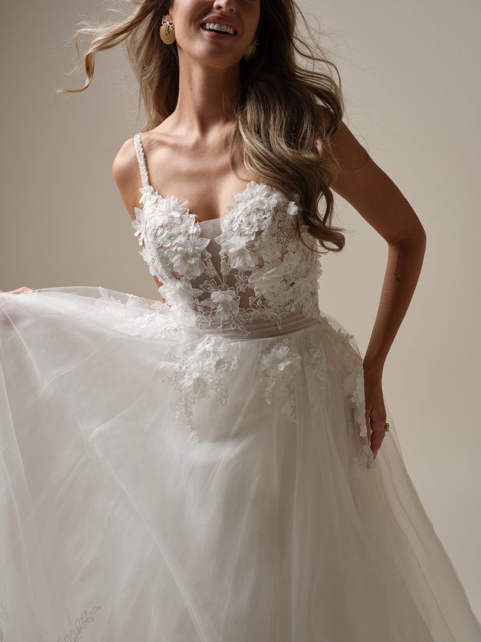 Close-up of a sheer bodice ballgown featuring 3D floral lace, beaded straps, and layered tulle skirt, styled with gold statement earrings and loose waves.