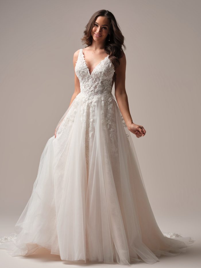 Bride in a romantic A-line wedding gown featuring a deep V-neckline, illusion lace bodice with floral embroidery, and a soft tulle skirt.