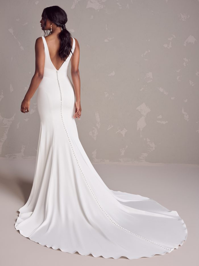 Bride wearing a fit-and-flare crepe wedding dress with a deep V-back and fabric-covered buttons trailing down a soft chapel-length train.