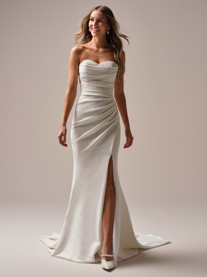 Bride wearing Kathleen by Rebecca Ingram, a casual stretch crepe sheath wedding dress with cowl sweetheart neckline, pearl accents, and side slit.