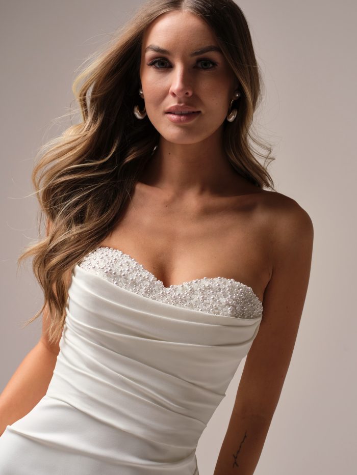 Close-up of Kathleen by Rebecca Ingram wedding dress with pearl-accented cowl sweetheart neckline and ruched crepe bodice.
