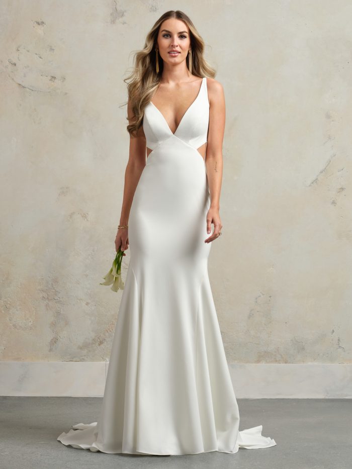 Front view of a crepe sheath wedding gown featuring a plunging V-neckline, cutout sides, and sleek silhouette, styled with soft curls and long statement earrings.
