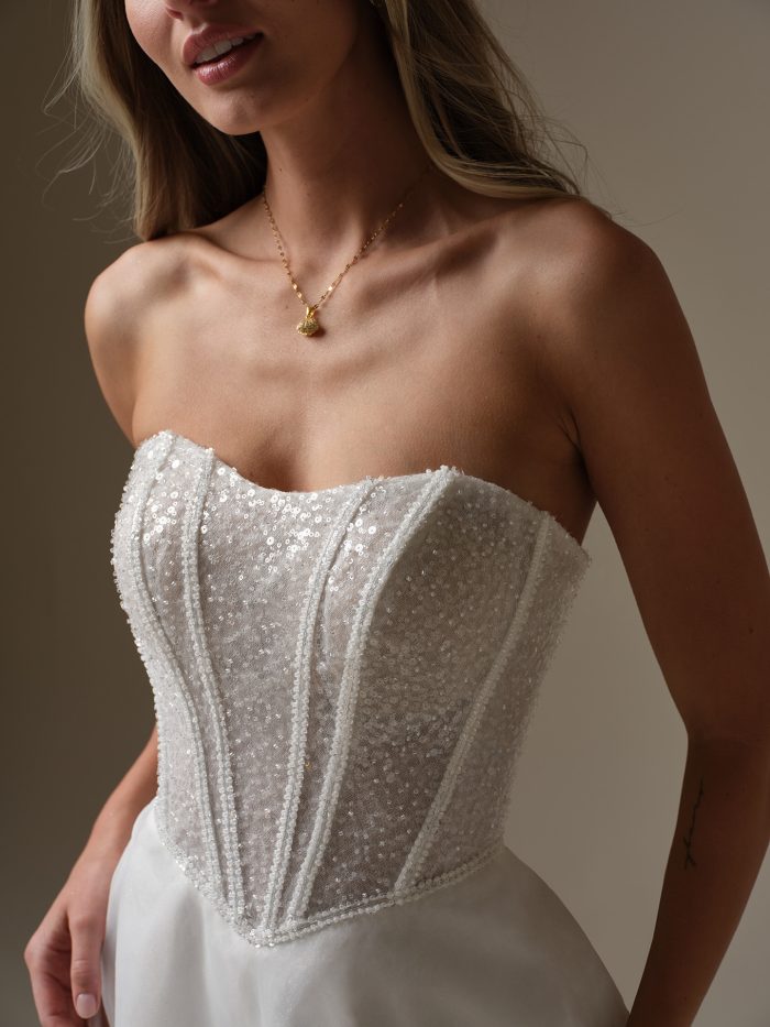 Close-up of a strapless wedding dress bodice featuring intricate sequin embellishments and exposed boning for a structured, modern look.