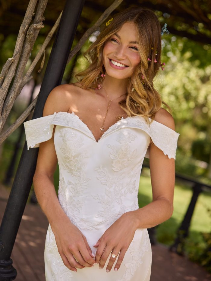 Close-up of the Miley fit-and-flare wedding dress by Rebecca Ingram, showcasing an off-the-shoulder sweetheart neckline and delicate floral lace appliqués.