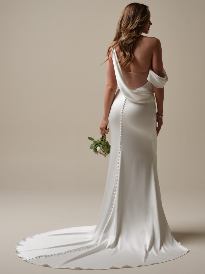 Back view of Nadia by Rebecca Ingram satin sheath wedding dress with draped one-shoulder strap, illusion V-back, and covered buttons down the train.