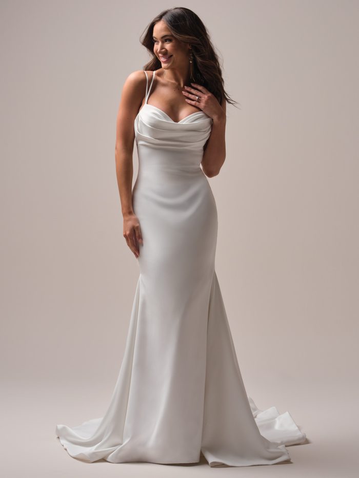 Bride wearing a slinky satin sheath wedding dress with a cowl neckline, double spaghetti straps, and soft sweeping train, styled with loose curls and statement earrings.
