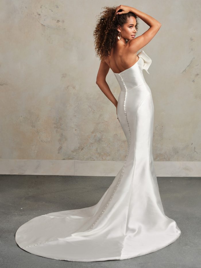 Back view of the Rebecca Ingram Pezy wedding dress featuring a sleek fit-and-flare silhouette with satin fabric, button detailing, and a dramatic train.