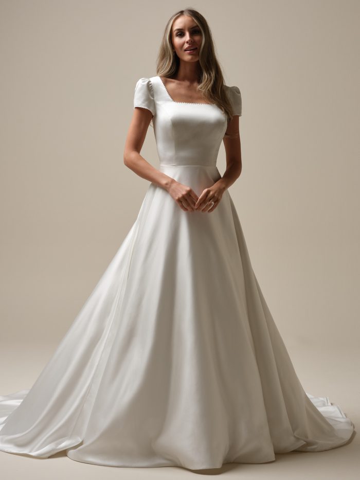 Bride wearing a classic satin A-line wedding dress with a square neckline, pearl-trimmed puff sleeves, and a full skirt—elegant and timeless with a hint of vintage charm.