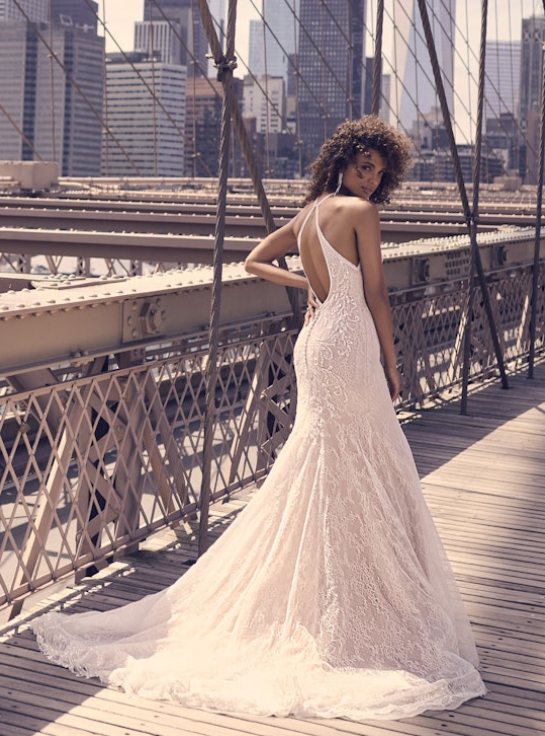 Back view of the Sloan sheath wedding dress, featuring an open halter back, beaded lace detailing, and a soft train, photographed on the Brooklyn Bridge with the city skyline in the background.