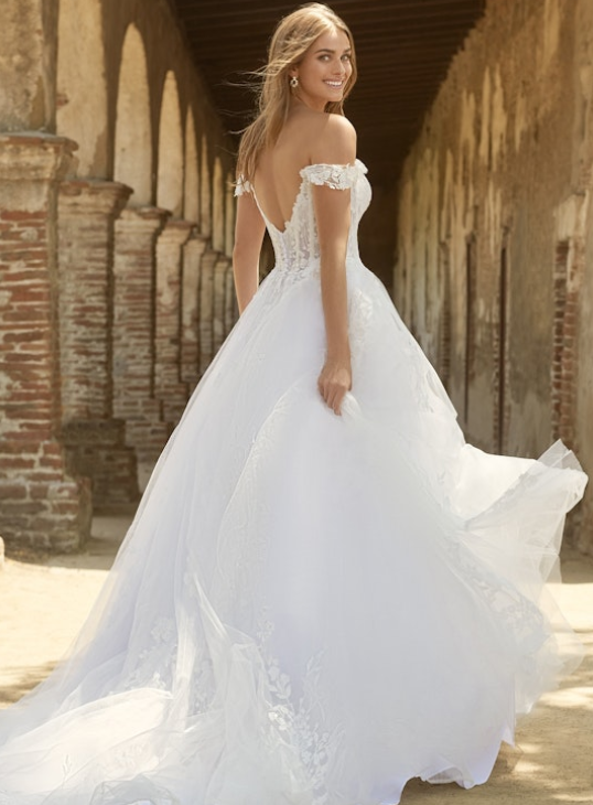 Back view of an off-the-shoulder lace ballgown wedding dress featuring a sheer corset back, floral appliqués, and a voluminous layered tulle skirt with a chapel-length train.