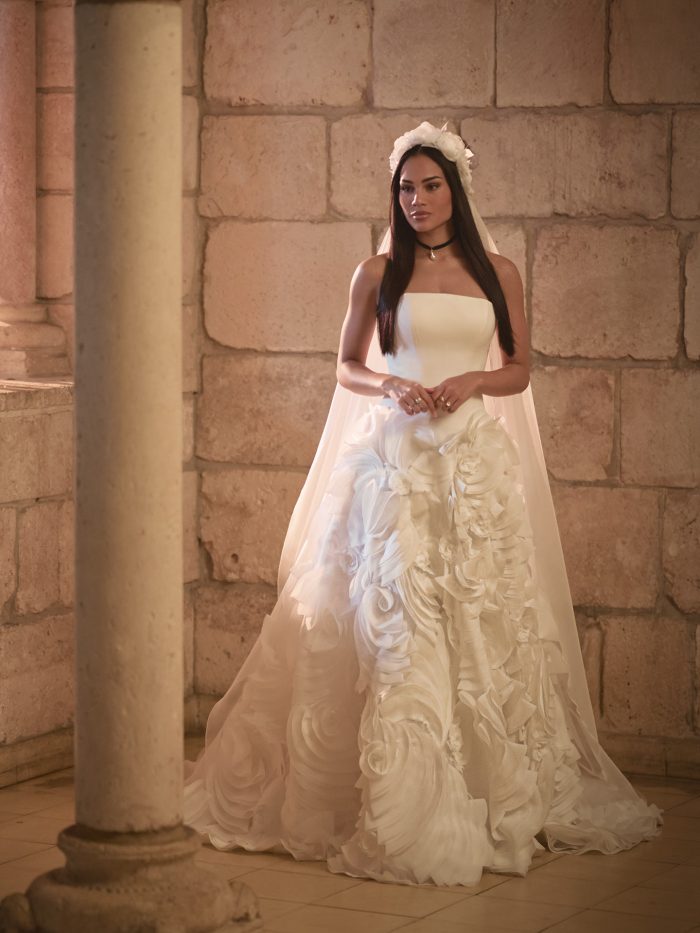 Bride wears Aarti by Sottero and Midgley—a statement ballgown with a structured bodice, voluminous floral-textured skirt, detachable cape, and bold accessories including a black choker and floral headpiece.
