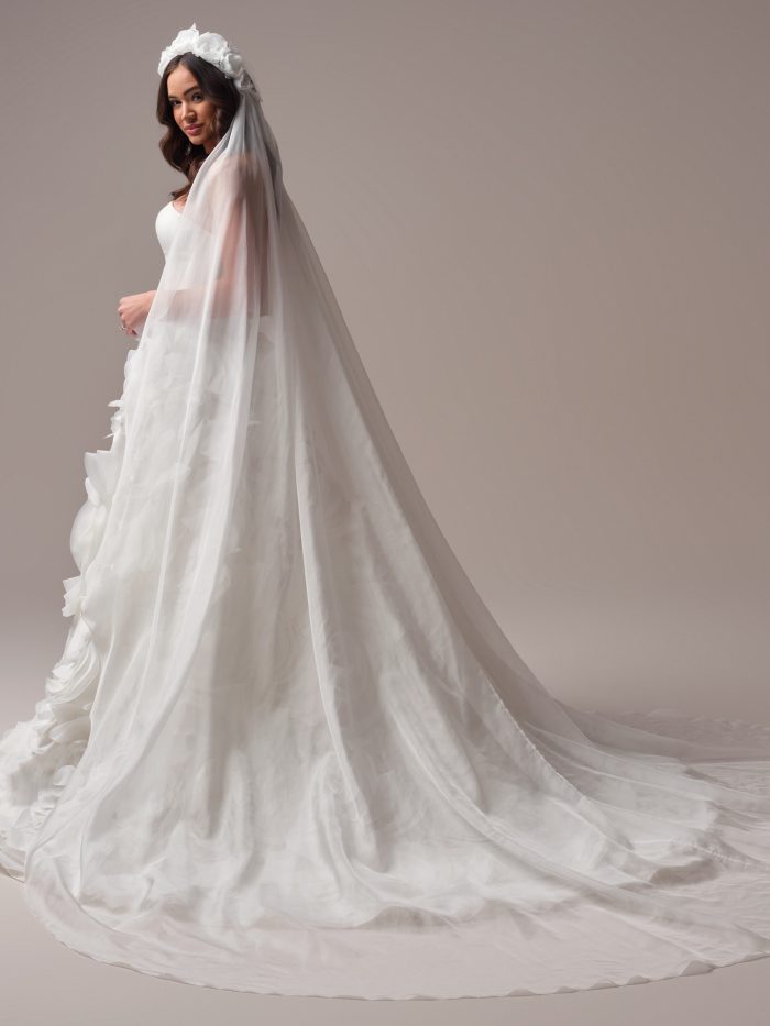Sottero and Midgley Aarti cathedral veil featuring sheer tulle and a dramatic silhouette, styled with a voluminous floral headpiece. A minimalist long veil that pairs effortlessly with statement gowns for a bold, fashion-forward bridal look