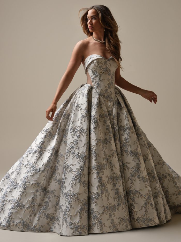 Bride wearing the Aberdeen ball gown wedding dress featuring a strapless sweetheart neckline, structured bodice, and voluminous skirt in textured blue and gold floral brocade.