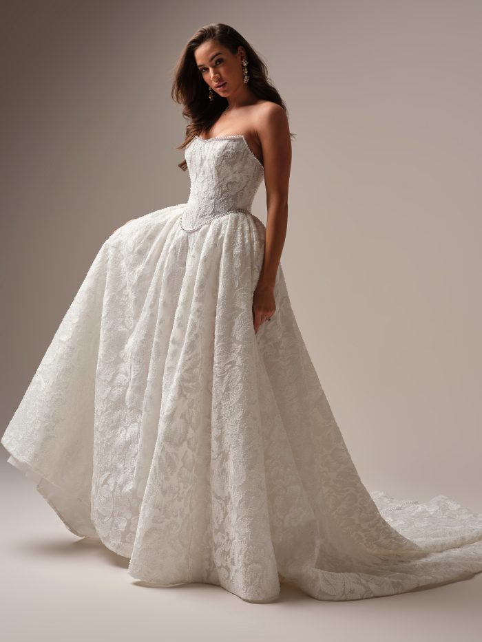 Bride wearing a strapless beaded ballgown wedding dress with a textured floral pattern, pearl-trimmed neckline, and voluminous skirt with a chapel-length train.
